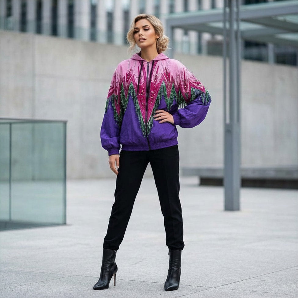 A woman stands outdoors wearing a colorful zip-up hoodie with a pink, purple, and green mountain pattern, paired with black pants and black ankle boots.