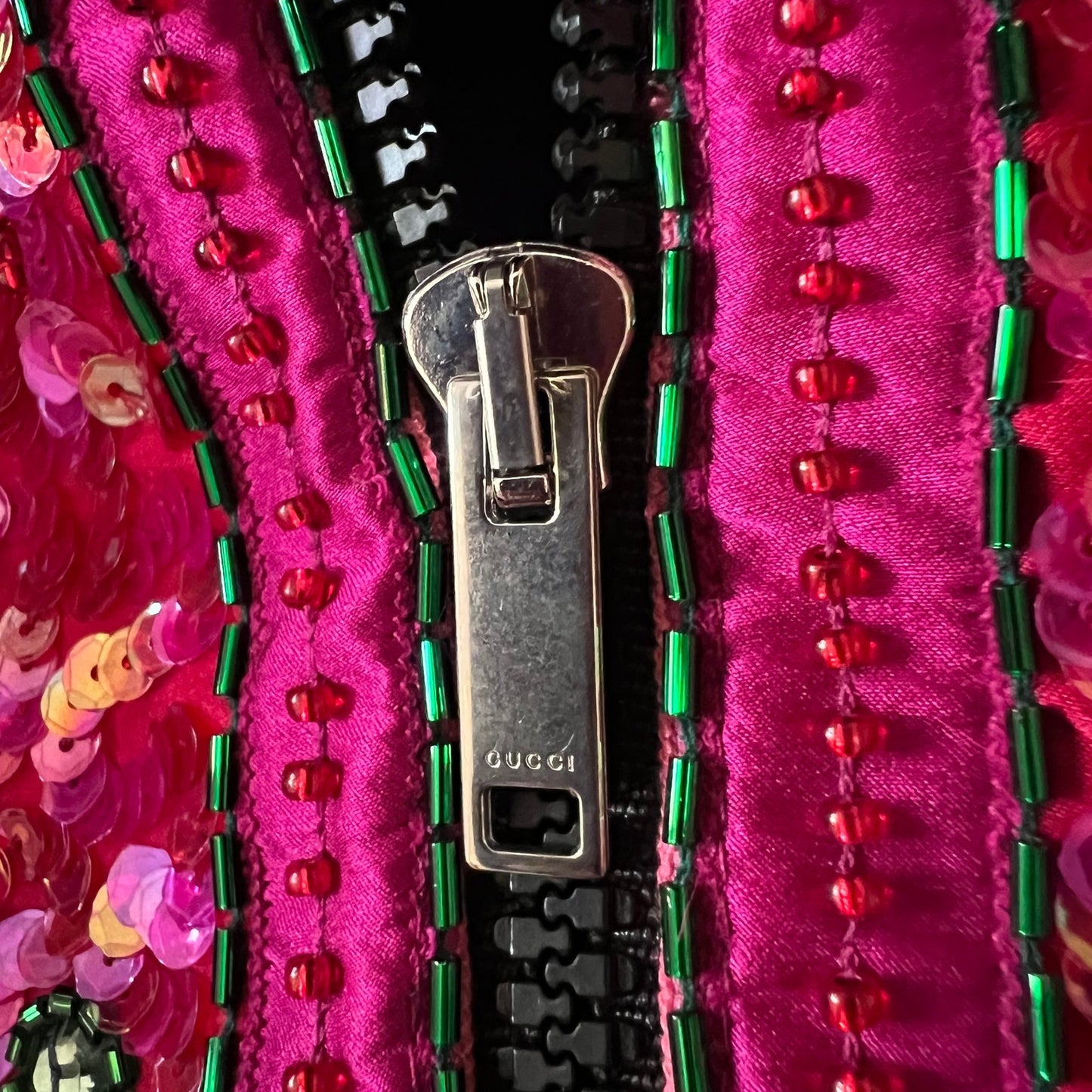 Close-up of a Gucci zipper pull on a vibrant magenta pink fabric adorned with green beads, red sequins, and sequined trim.
