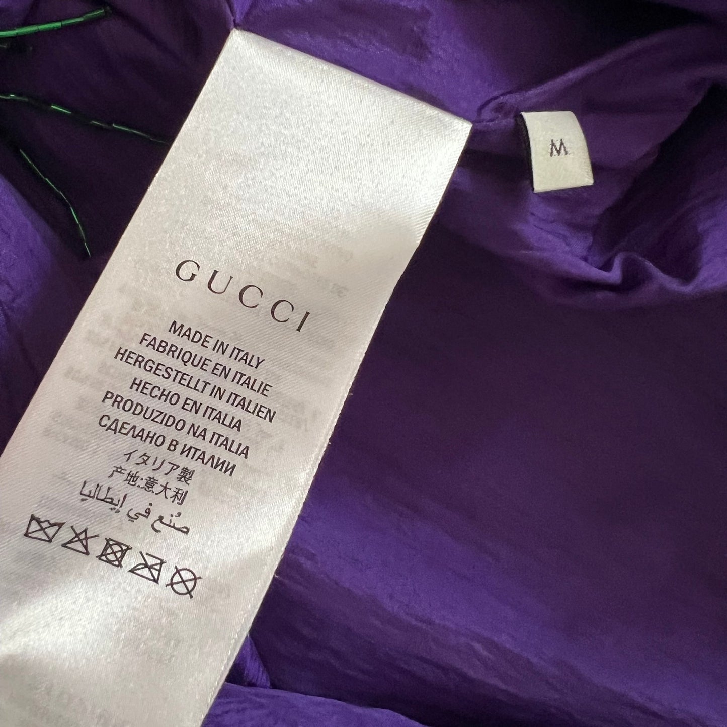 Close-up of a purple garment interior showing a white Gucci care label and a small size tag marked M.
